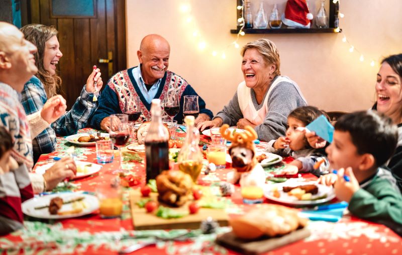 Mehrgenerationenfamilie lacht und genießt ein festliches Weihnachtsessen an einem dekorierten Tisch, symbolisch für genussvolle Feiertage ohne Verdauungsbeschwerden.